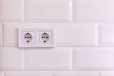 Group of two white european electrical outlets on a wall of white tile in a modern kitchen or bathroomの写真素材