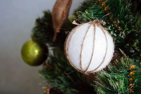 A white ball wrapped in a waxed cord hangs on an artificial Christmas tree decorated in rustic styleの写真素材