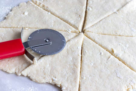 Rolled raw curd dough cut into eight triangles with a red round pizza knife on it on baking paper. The process of making curd bagels or croissants. Closeup viewの写真素材