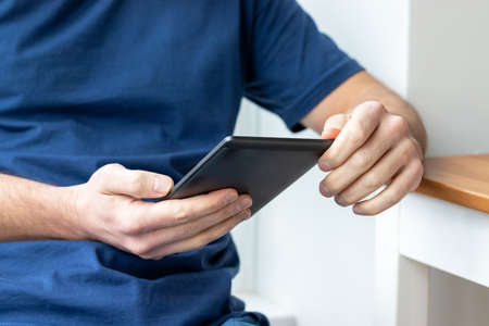 Gray e-reader electronic book in male hands. A man in a blue t-shirt with a tablet. Selective focusの写真素材