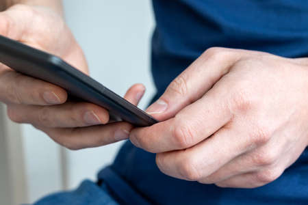 Gray e-reader electronic book in male hands. A man in a blue t-shirt with a tablet. Selective focusの写真素材