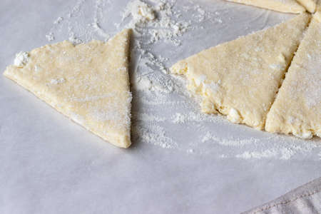 Rolled raw curd dough cut into eight triangles sprinkled with sugar and one triangle of dough lies separately on baking paper on a linen tablecloth. The process of making curd bagels or croissantsの写真素材