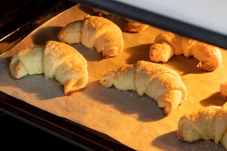 Oven-baked sugar-frosted croissants on a baking sheet covered with parchment paper. Sweet bagels from a cottage cheese dough baked in a hot oven. The process of making curd bagels or croissantsの写真素材