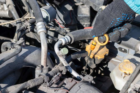 Man checking oil level under the open hood of a flat-four (boxer) car engine compartment. Closeup view on a sunny dayの写真素材