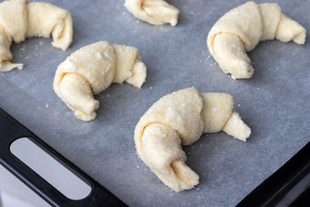 Croissants from a raw cottage cheese dough prepared for baking sprinkled with sugar on a baking sheet covered with parchment baking paper before loading into the oven. Process of making curd bagelsの写真素材
