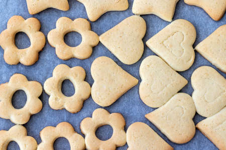 Baked shortbread cookies in the form of hearts and flowers on a baking sheet with parchment paper just taken out of the oven. Tea snack for breakfast. Selective focus. Closeup viewの写真素材