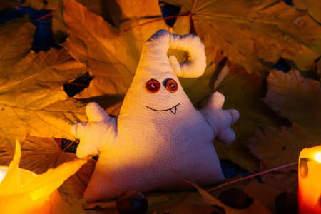 A toy monster with button eyes sits among leaves and candlesの写真素材