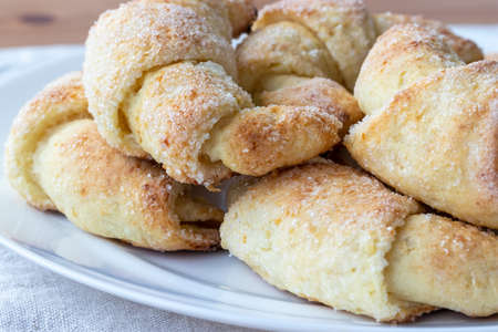 Sugar-frosted croissants from a cottage cheese dough on a white plate on a gray linen tablecloth just taken out of the oven. Tea snack for breakfast. The process of making curd bagels or croissantsの写真素材