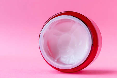 Round open red plastic jar with with white cream inside on a pink background with copy space. Skin care, cosmetics concept. Beauty packaging template. Side closeup viewの写真素材