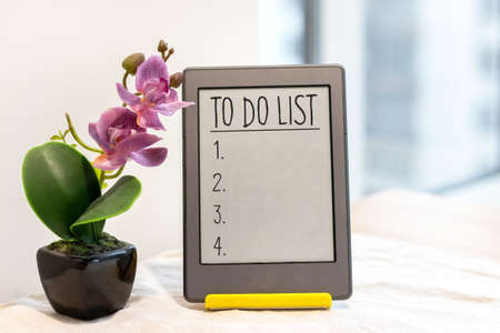 To do list in gray tablet on a yellow stand next to an artificial pink orchid on the kitchen table with a linen tablecloth by the windowの写真素材