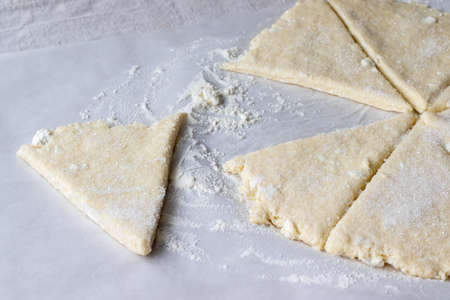 Rolled raw curd dough cut into eight triangles sprinkled with sugar and one triangle of dough lies separately on baking paper on a linen tablecloth. The process of making curd bagels or croissantsの写真素材