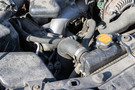 Dusty details of a flat-four (boxer) car engine compartment under the open hood. Car radiator cap and hose. Closeup view on a sunny dayの写真素材