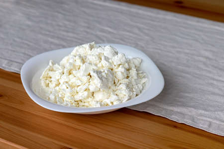 A white square plate filled with cottage cheese stands on a linen tablecloth on a wooden table. Selective focusの写真素材