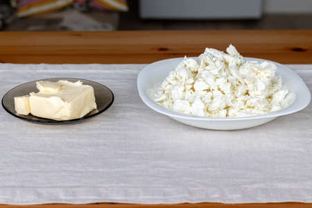 A white square plate with cottage cheese and brown transparent plate with butter stands on a linen tablecloth on a wooden table. The process of making curd bagels or croissantsの写真素材