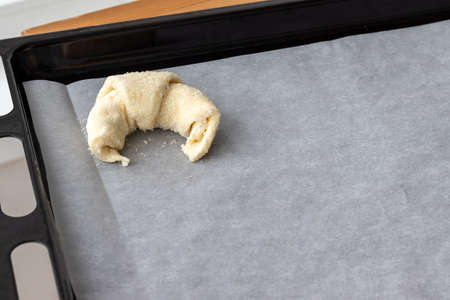 One croissant prepared for baking from a curd dough sprinkled with sugar on a parchment paper on a baking sheet. Sweet bagel before loading into the oven. Process of making curd bagels or croissantsの写真素材