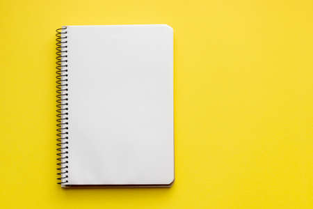 Spiral notebook with blank empty white sheets on a bright yellow background, top view, flat lay with copy spaceの写真素材