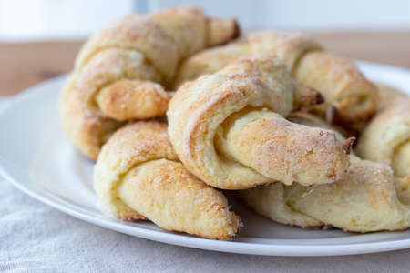 Sugar-frosted croissants from a cottage cheese dough on a white plate on a gray linen tablecloth just taken out of the oven. Tea snack for breakfast. The process of making curd bagels or croissantsの写真素材