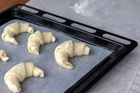 Croissants from a raw cottage cheese dough prepared for baking sprinkled with sugar on a baking sheet covered with parchment baking paper before loading into the oven. Process of making curd bagelsの写真素材