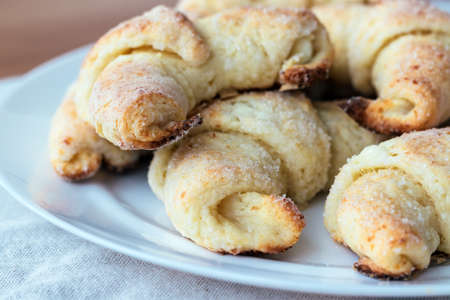 Croissants from a cottage cheese dough on a white plate on a gray linen tablecloth just taken out of the oven. The process of making curd bagels or croissants. Selective focus. Closeup viewの写真素材