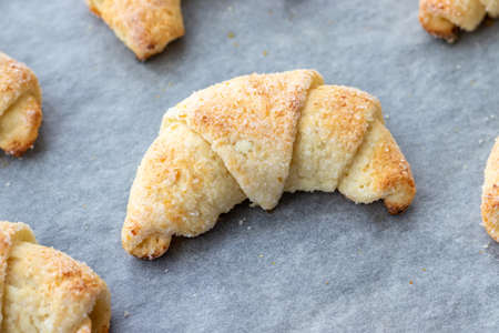 Baked croissants from a cottage cheese dough with sugar on a baking sheet with parchment paper just taken out of the oven. Tea snack for breakfast. The process of making curd bagels or croissantsの写真素材