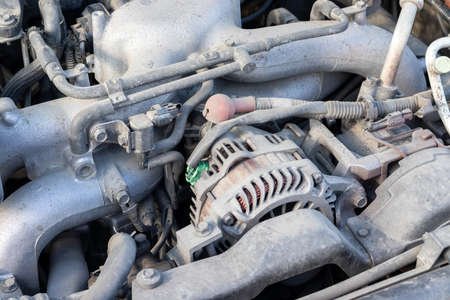 Dusty details of a flat-four (boxer) car engine compartment under the open hood. Alternator and intake manifold. Closeup viewの写真素材