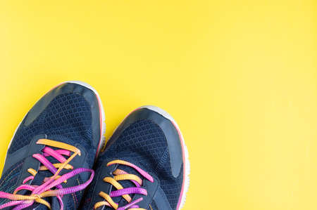 Dark blue sneakers with multicolored pink, purple, yellow laces on a bright yellow background with copy space. Concept of sports, fitness, workout, runningの写真素材