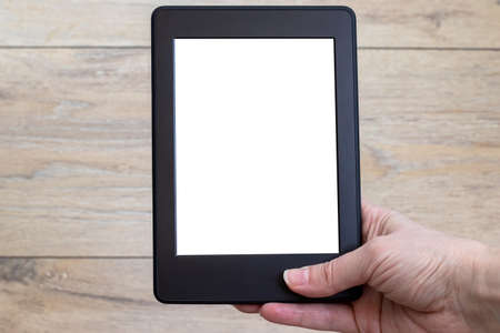 A modern black electronic book with a white empty blank screen in female hand against a blurred wooden background. Mockup tablet template closeupの写真素材