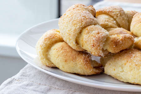 Sugar-frosted croissants from a cottage cheese dough on a white plate on a table with linen tablecloth. Tea snack for breakfast. The process of making curd bagels or croissants. Selective focusの写真素材