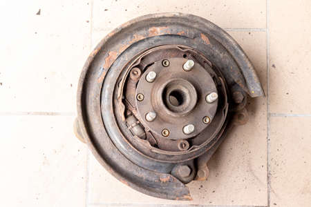 Old, used, rusty rear hub, on which the brake pads of the parking brake are visible, without brake disc on the beige tiled floor of the workshopの写真素材