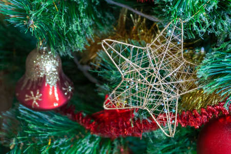Green artificial Christmas tree decorated with star in a golden frame and interlacing golden threads; red bell with gold glitter; and yellow and red garlands. Home decoration for a family holidayの写真素材