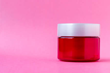 Round red plastic jar with a white cap on a pink background with copy space. Skin care, cream, cosmetics concept. Beauty packaging mockup template. Side viewの写真素材