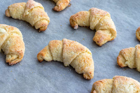 Baked croissants from a cottage cheese dough with sugar on a baking sheet with parchment paper just taken out of the oven. Tea snack for breakfast. The process of making curd bagels or croissantsの写真素材