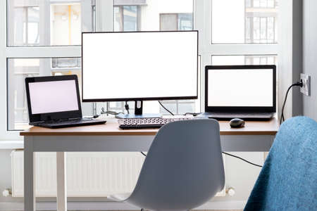 Bright workplace with two laptops and a monitor with white mockup empty screens near the window. Remote work from home in quarantineの写真素材