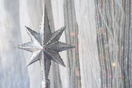 Silver Christmas star with many sparkles against a light textile curtain. Home decoration for a family holiday with copy space. Christmas tree top. Selective focusの写真素材