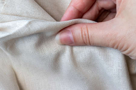 Natural linen fabric in woman hand. Rough crumpled burlap. Selective focus. Closeup viewの写真素材