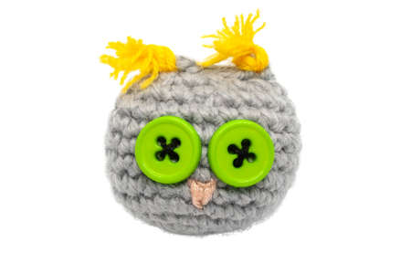 Small crocheted (knitted) owl toy of gray threads with yellow ears, a pink nose and eyes of green buttons isolated on a white background without shadowの写真素材