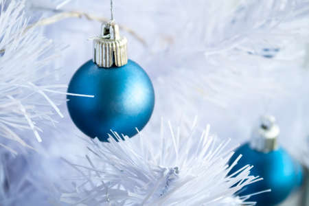 Closeup view of a blue matte ball hanging on a silver thread on a white artificial Christmas tree. Selective focus. Blurred backgroundの写真素材