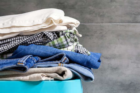 Folded bedding, jeans, towels on a blue box against the blurred background of a gray concrete wall in the bathroom. Pile of laundry and clothes prepared for washing. Closeup viewの写真素材