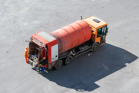 Modern orange gas-powered garbage truck with a cylinder tank for compacting garbage with two workers against gray asphalt, top viewのeditorial素材