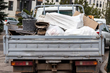 An open truck body filled with various rubbish, bags, cardboard, construction waste, rear view. Garbage collection after repair and construction of buildingsの写真素材