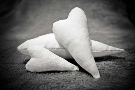 Three soft handmade hearts sewn from flax, lie on the rug. Vignetted black and white photo with cinematic grainの写真素材