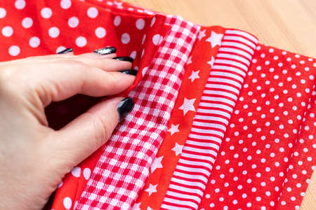 Female hand on a pile of five types of red and white cotton fabrics with different prints:...