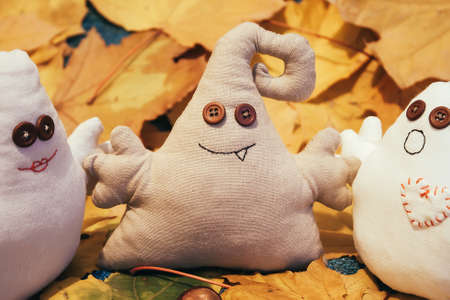 Three toy monsters with button eyes sit among leavesの写真素材