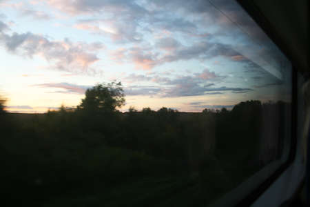 An evening landscape with a setting sun and beautiful clouds is seen through a large train windowの写真素材