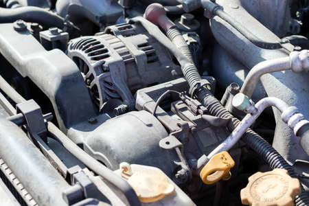Dusty details of a flat-four (boxer) car engine compartment under the open hood. Alternator and intake manifold. Closeup side view on a sunny dayの写真素材