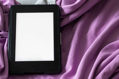 A modern black e-reader electronic book with a blank screen on a gray and purple bed. Mockup template tablet on microfiber bedding closeupの写真素材