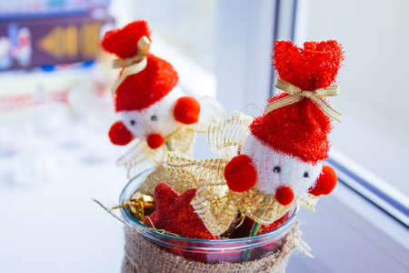 A vase stands at the window filled with red and yellow Christmas tree toys. Two snowmen on sticks are on top.の写真素材
