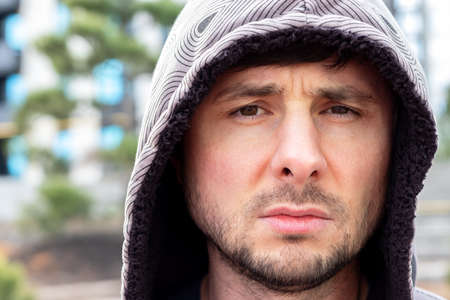 Serious handsome bearded man in a hood against a blurred background, closeup portraitの写真素材