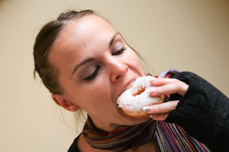 Beautiful woman in a multi-colored striped scarf, dark gray sweater and mittens bites a donut in white glazeの写真素材