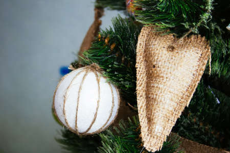 A white ball wrapped in a waxed cord and a heart sewn from sacking hang on an artificial Christmas tree decorated in rustic styleの写真素材